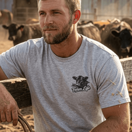 Man wearing a Farm Life T-Shirt, featuring a cow graphic, surrounded by cows in a ranch setting.
