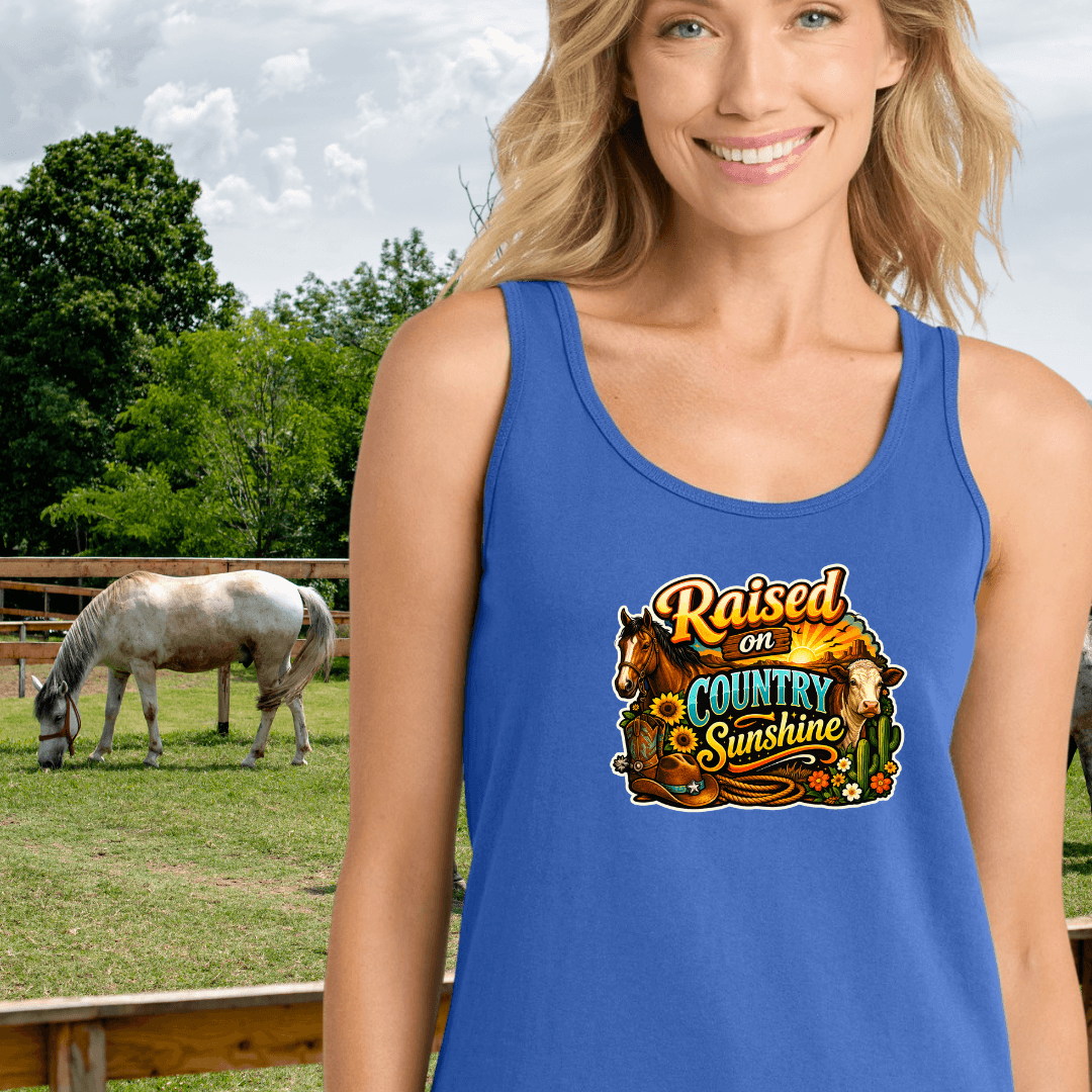 Woman wearing a blue Country Tank Top featuring the text 'Raised on Country Sunshine' with a horse in the background.